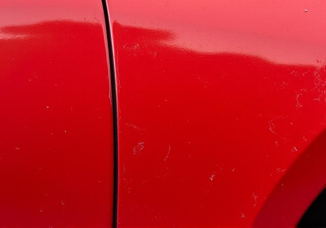 Dull, swirled red paintwork on a car door.